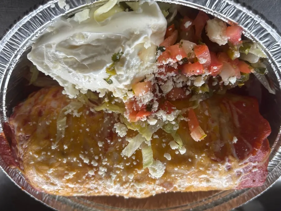 A mojado (wet) burrito smothered in red sauce and melted cheese, with lettuce, pico de gallo, cotija, and sour cream on the side