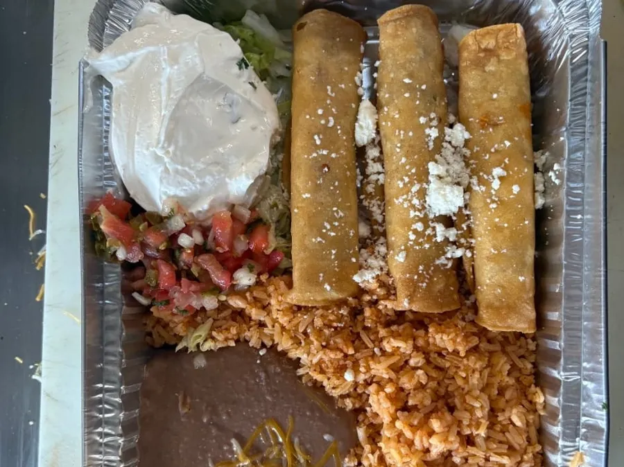 Flautas topped with cotija cheese, rice, and beans